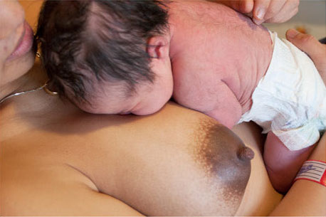 a baby sitting upright on mother's breast